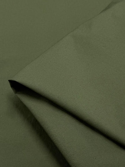 Close-up of a folded piece of "Mayfly" plain cotton by Super Cheap Fabrics, in dark olive green. Showcasing its smooth texture and simple design, the 145cm lightweight material is neatly arranged with visible folds, resembling the delicate grace of a mayfly's wings.