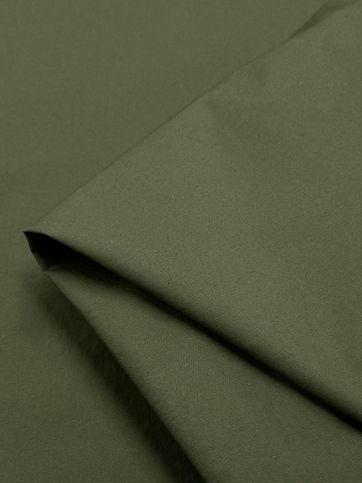 Close-up of a folded piece of "Mayfly" plain cotton by Super Cheap Fabrics, in dark olive green. Showcasing its smooth texture and simple design, the 145cm lightweight material is neatly arranged with visible folds, resembling the delicate grace of a mayfly's wings.