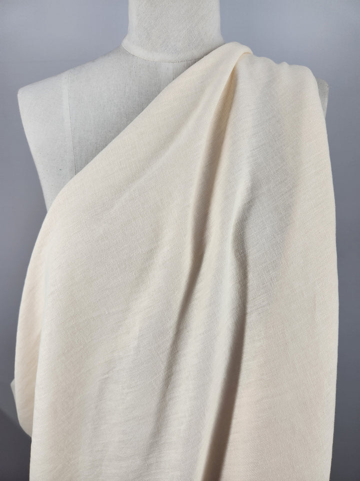 A mannequin is draped in Super Cheap Fabrics' Pure Washed Linen - Eggnog - 140cm, highlighting its lightweight, soft texture and slight sheerness. The gentle folds convey elegance and movement reminiscent of pure linen.