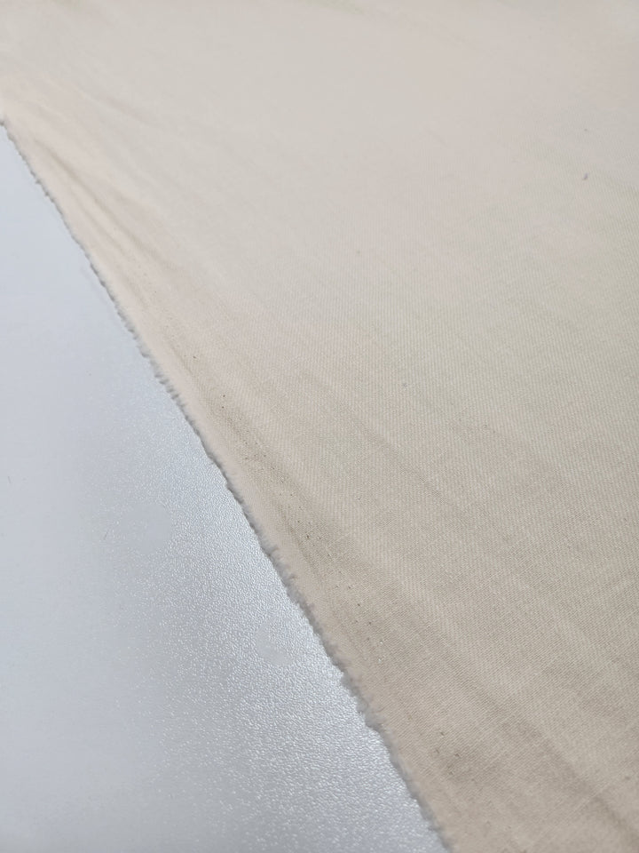 A close-up of the lightweight Pure Washed Linen in Eggnog by Super Cheap Fabrics, showing its rough edge on a smooth white surface, contrasting textures vividly evident.