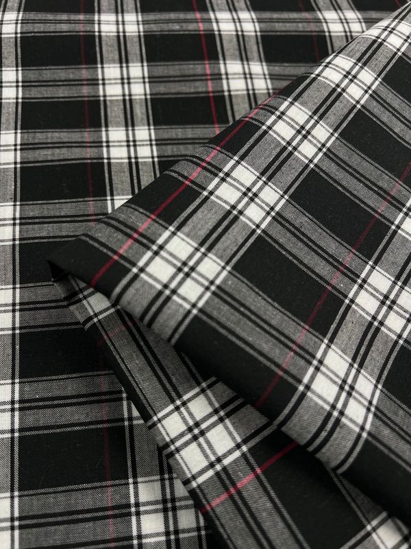 Close-up of neatly stacked layers of the Douglas Shirting fabric from Super Cheap Fabrics, featuring folded black, white, and red plaid in a classic checkered pattern. This lightweight polyester cotton fabric beautifully showcases an intricate interplay of colors and lines, making it perfect for multiuse clothing. Width: 150cm.