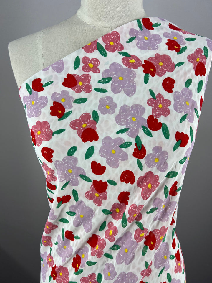 The Salt Shrunk Print - Daise - 155cm by Super Cheap Fabrics is elegantly draped on a mannequin, featuring vibrant red, purple, and pink floral patterns against green leaves on a crisp white background.