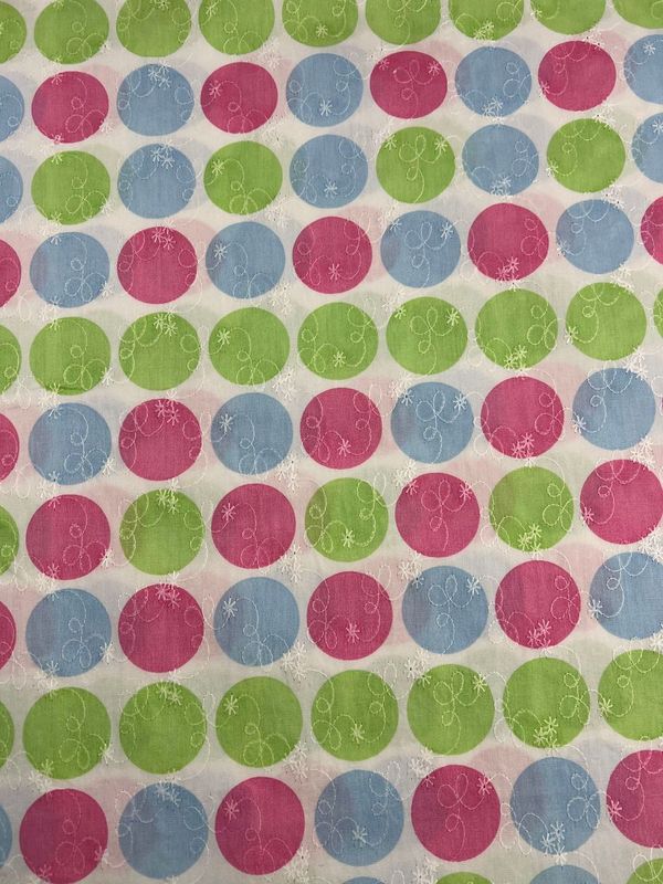 The 'Embroidered Printed Cotton - Candy - 112cm' by Super Cheap Fabrics features a lively polka dot design with pink, green, and blue circles enhanced by white snowflake-like patterns. Crafted from natural cotton fibers, this fabric is ideal for making clothing and household items with its fresh white background.