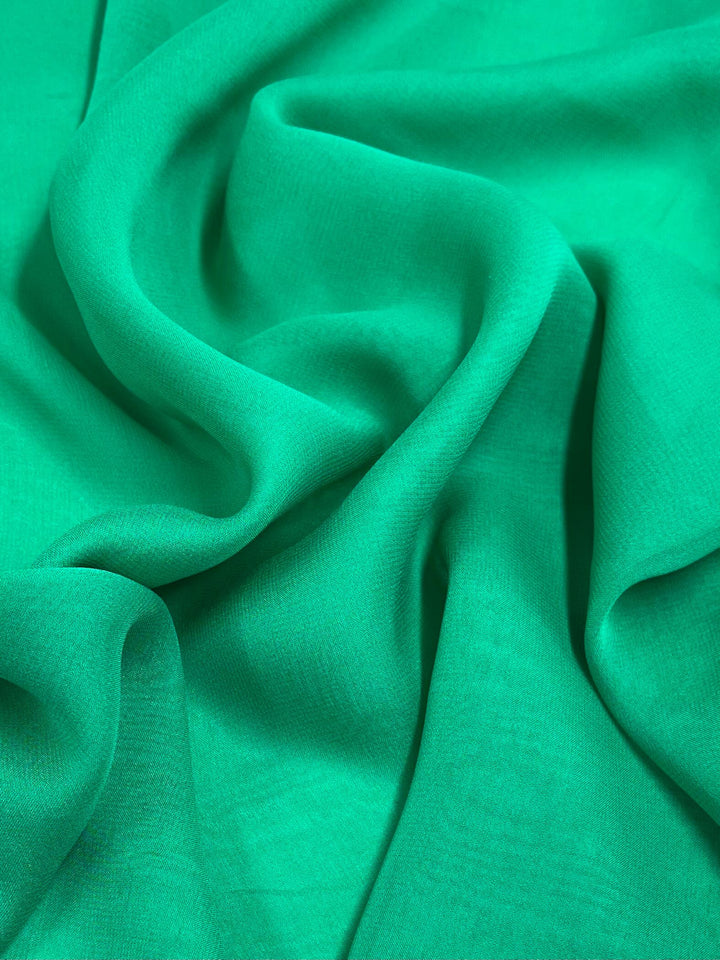 A close-up of the Super Cheap Fabrics' Silk Georgette in Emerald, measuring 135cm, showcasing its soft and smooth texture with gentle folds and drapes.