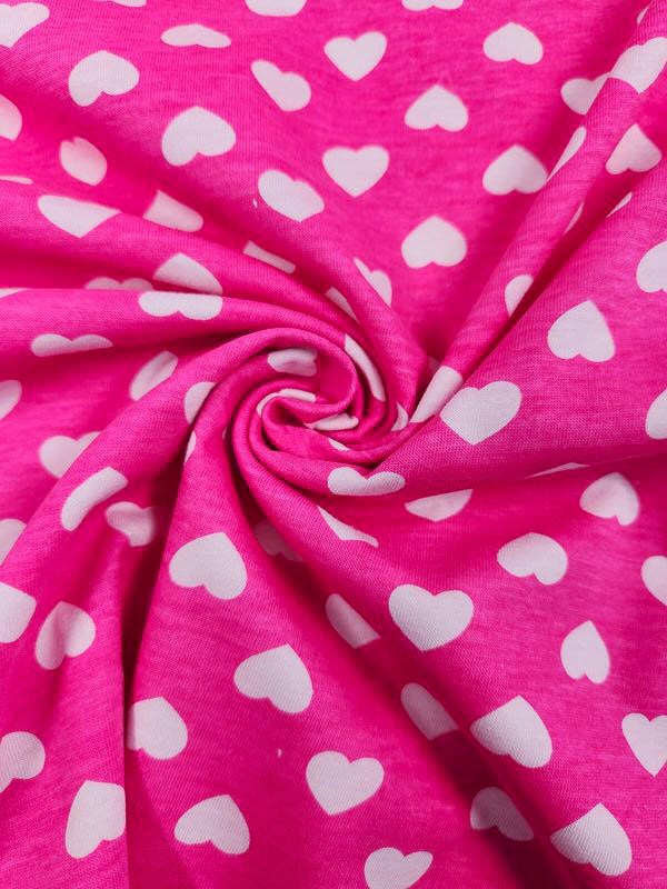 Close-up of Super Cheap Fabrics' Printed Jersey - Hearts, 160cm. This medium-weight fabric features a white heart pattern on pink and is gathered at the center to create a spiral-like design.