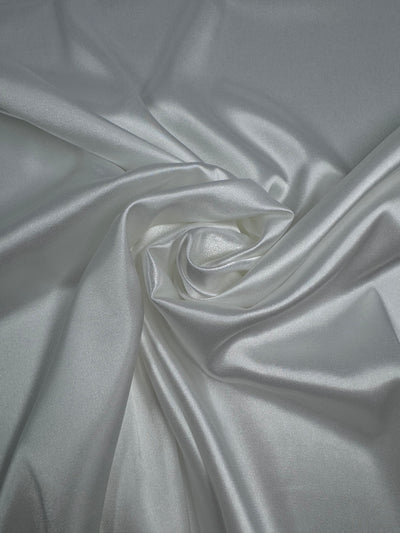 Satin Deluxe - Ivory - 150cm by Super Cheap Fabrics features smooth, shiny satin fabric arranged in gentle folds with a lustrous finish, reflecting light for a beautiful, silky appearance.
