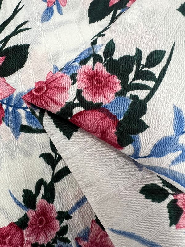 A close-up of Super Cheap Fabrics' Textured Deluxe Print - Catch The Bouquet shows designer fabric with pink flowers and green leaves on white. The 155cm versatile textile is layered to highlight its pattern and texture.