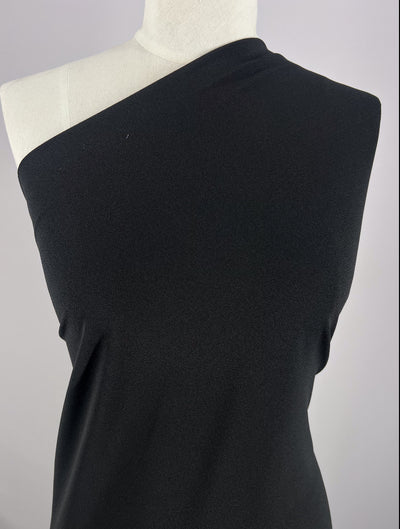 A mannequin wears a one-shoulder garment made from Super Cheap Fabrics' Plain Lycra - Black - 165cm, exposing the right shoulder and covering the left, set against a plain light background.
