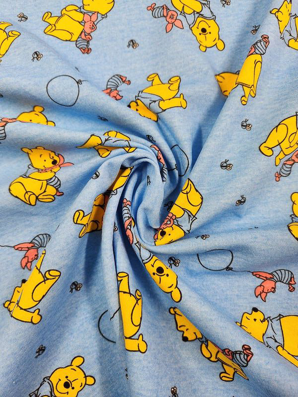 The Super Cheap Fabrics Printed Jersey - Winnie & Co - 170cm features a playful design with cartoon bears, piglets holding balloons, and wearing scarves on a blue background. Gathered at the center, this poly/cotton blend fabric highlights its charming pattern.