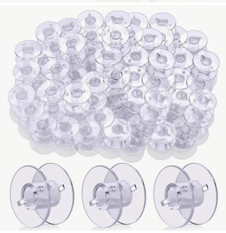 A collection of the Super Cheap Fabrics "Bobbins With Case 25" transparent suction cups, similar to clear empty bobbins, is neatly arranged in piles and rows. Each cup has a small pull tab and is set against a plain white background.