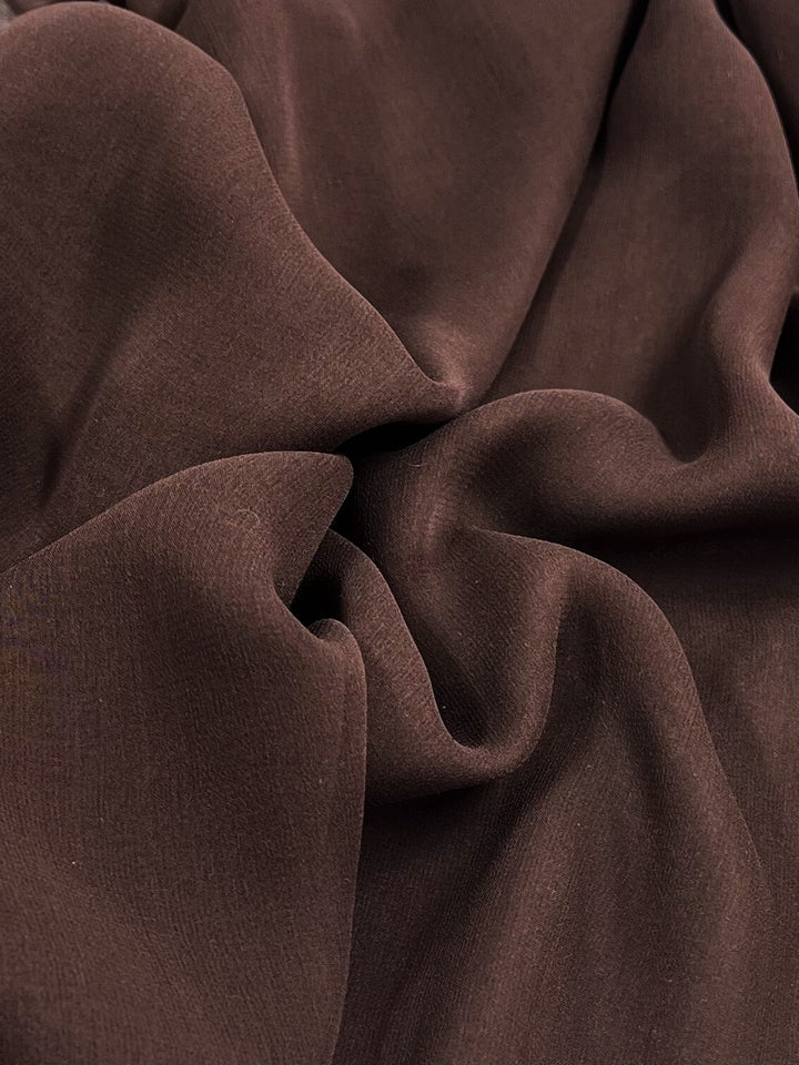 A close-up of Super Cheap Fabrics' Pure Silk Georgette in Chocolate (135cm) draped in soft folds, crafting gentle shadows and a smooth texture, ideal for spring and summer outfits.