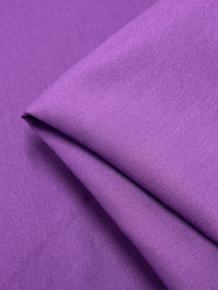 A close-up image of a piece of Super Cheap Fabrics' Plain Rayon - Iris Orchid - 140cm, with a smooth texture, folded neatly in the center. The fabric's lightweight weave and slight sheen are visible under the light.