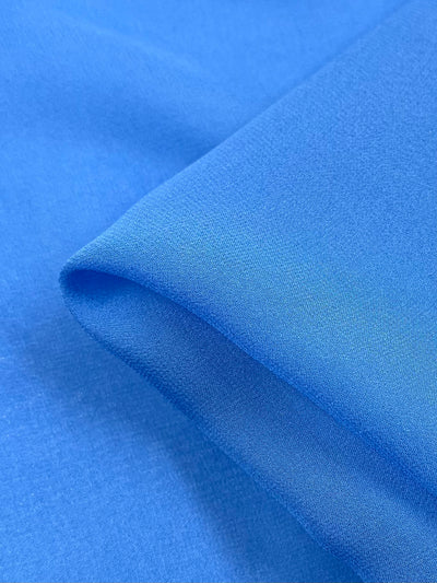 A close-up of Pure Silk Georgette - Denim by Super Cheap Fabrics reveals its smooth, light blue color with gentle folds, showcasing a soft texture and slight shine. The 135cm wide lightweight fabric is perfect for elegant spring-summer outfits.