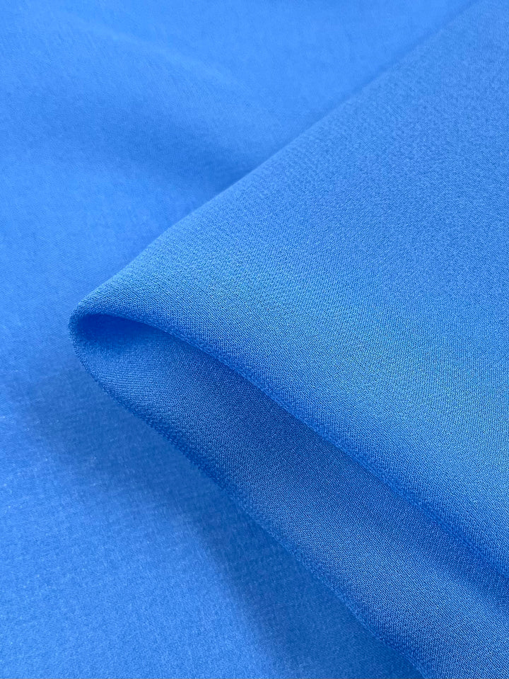 A close-up of Pure Silk Georgette - Denim by Super Cheap Fabrics reveals its smooth, light blue color with gentle folds, showcasing a soft texture and slight shine. The 135cm wide lightweight fabric is perfect for elegant spring-summer outfits.