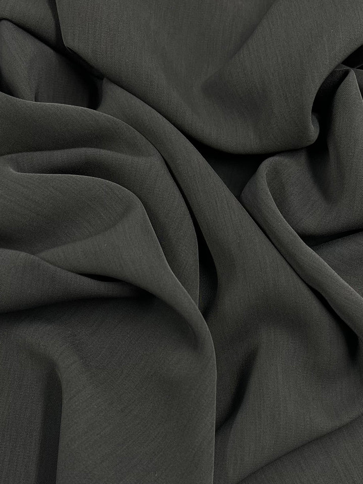 A close-up of soft, smooth, Microfibre Suiting - Charcoal - 150cm fabric with gentle folds and drapes. This medium weight polyester material from Super Cheap Fabrics, with a 150 cm width, appears silky and flows elegantly, creating a series of soft shadows and highlights across its surface.