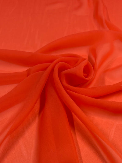 A smooth piece of Super Cheap Fabrics' Hi-Multi Chiffon - Coral Quartz - 150cm is draped and slightly gathered in a spiral at the center of the image. The lightweight material appears sheer, with soft folds and gentle shadows.