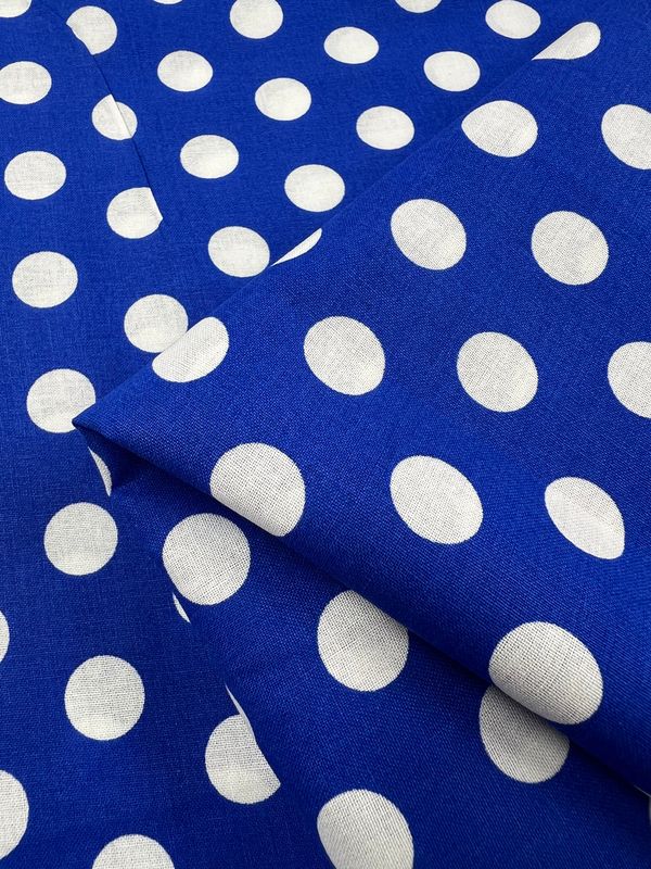 A close-up of Super Cheap Fabrics' Linen Blend - Dazzling Blue - 112cm, with large white polka dots. The lightweight fabric is slightly folded, highlighting its vibrant texture and design.