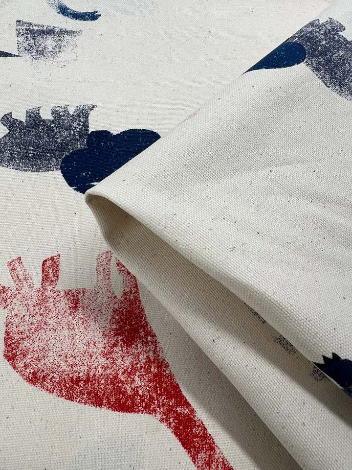 Close-up of medium-weight "Dino Art" printed canvas by Super Cheap Fabrics, featuring abstract animal-like red and blue shapes. The folded 113cm cotton fabric highlights its texture and pattern, ideal for home décor projects.