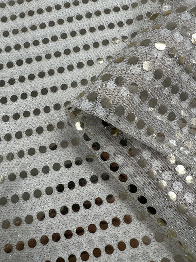 Close-up of the Sequin - White Gold - 112cm fabric from Super Cheap Fabrics, featuring a shiny black appearance with a silver base and metallic circular sequins evenly spaced throughout. The dancewear fabric is slightly folded, creating an eye-catching shine as light reflects off the sequins.