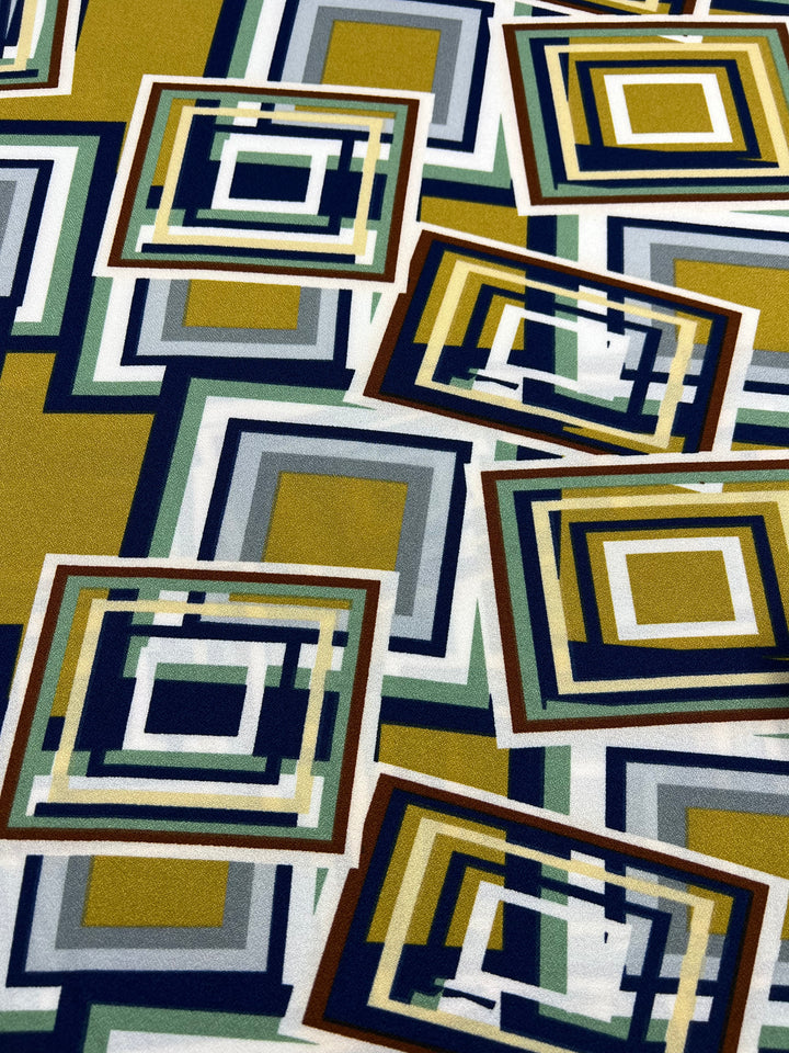 Super Cheap Fabrics' Printed Crepe - 3D Squares - 150cm features a geometric pattern of overlapping squares in green, yellow, blue, and white. This abstract design is ideal for creating high-fashion pieces with its layered effect and lightweight polyester material.