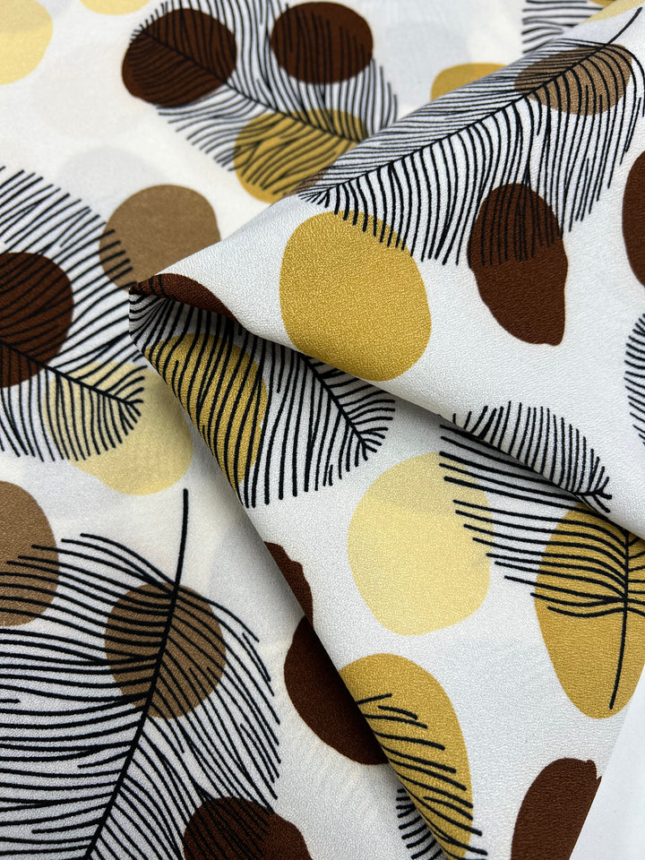 Close-up of Super Cheap Fabrics' Printed Crepe - Brown Dotty Leafs (150cm). This high-fashion, lightweight fabric features large overlapping circles in brown, yellow, and beige with black feathery lines for a textured look on a smooth background.