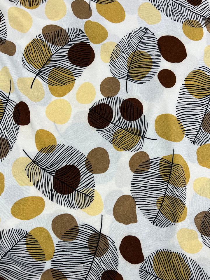 The Printed Crepe - Brown Dotty Leafs by Super Cheap Fabrics is a high-fashion, lightweight polyester fabric. It features an abstract pattern of brown, yellow, and beige leaves with black outlines on a white background adorned with overlapping circles for a textured effect. Width: 150cm.