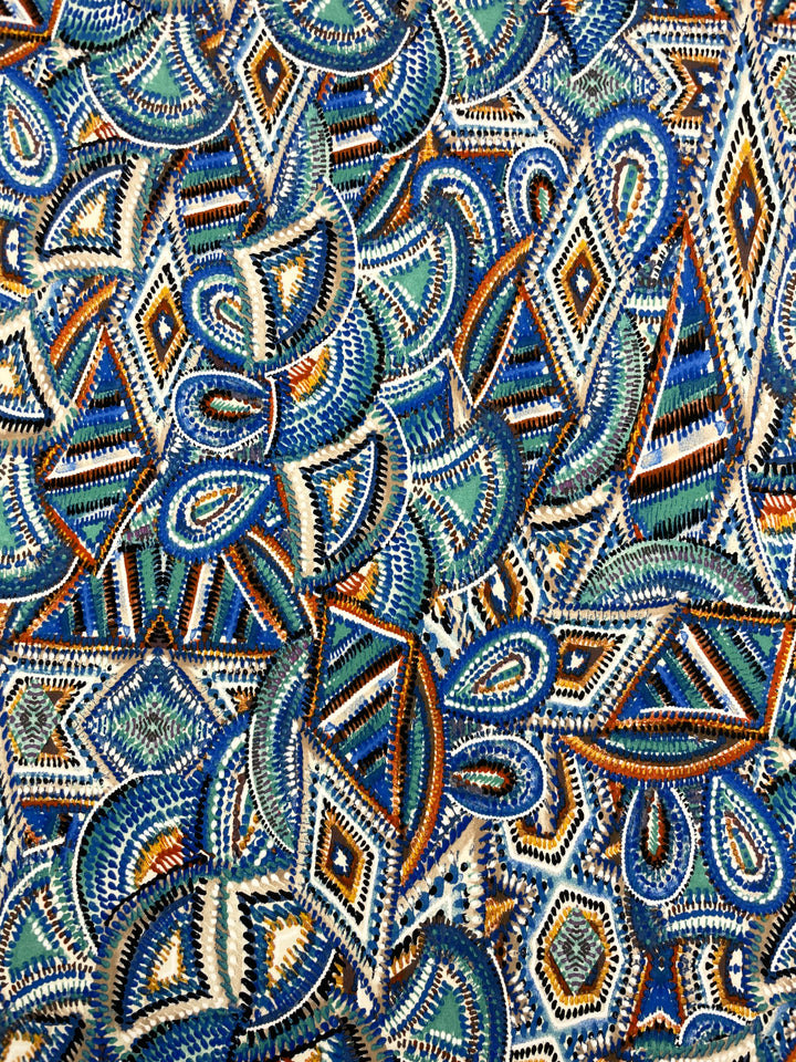 Introducing the "Printed Lycra - Mirage - 150cm" by Super Cheap Fabrics, an intricately designed, colorful textile. This polyester spandex fabric showcases swirling geometric patterns, including diamonds, circles, and zigzags in vibrant shades of blue, white, green, and orange. The medium weight fabric is densely packed and highly detailed.