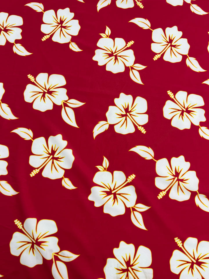 The Printed Nylon Lycra - Tropical from Super Cheap Fabrics features bright cranberry fabric adorned with white hibiscus flowers with yellow centers and simple leaf designs, offering a lively and tropical look that's perfect for cheerful sportswear.