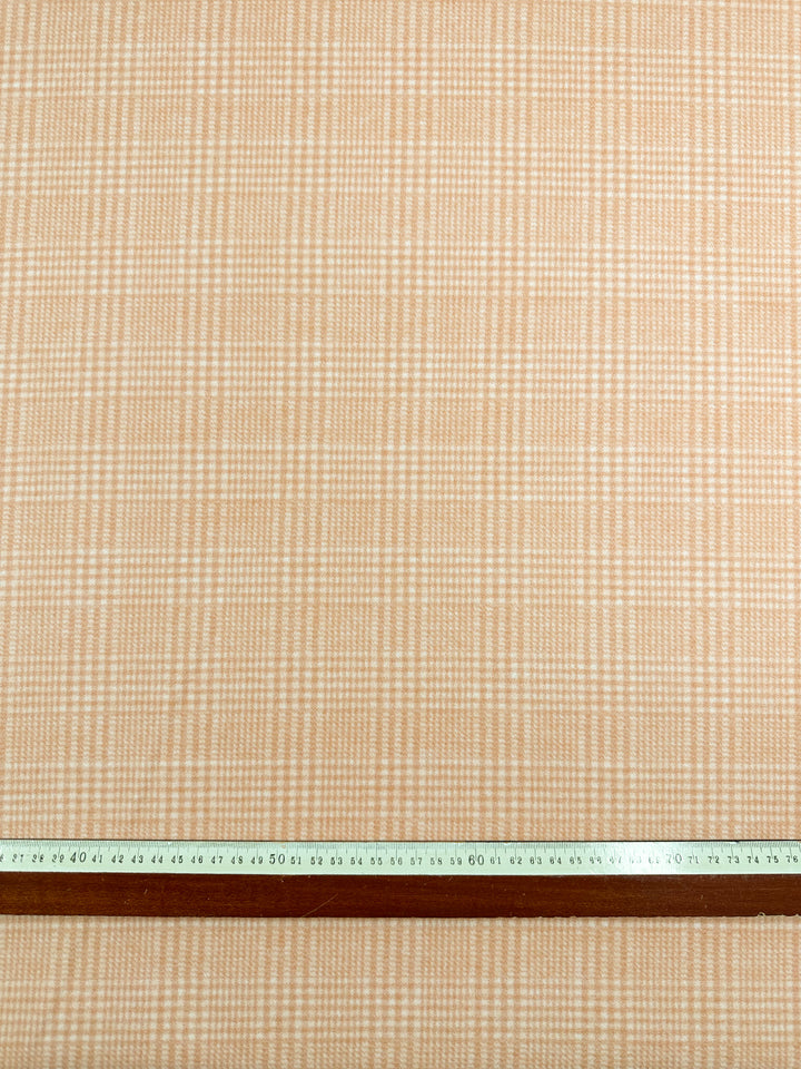 A close-up view of beige and white plaid flannel fabric with a wooden ruler placed horizontally at the bottom. The ruler has both centimeter and inch markings visible, showing a length of up to 60 centimeters and approximately 24 inches. The fabric featured is Wool Flannel - Mandarin - 148cm from Super Cheap Fabrics.