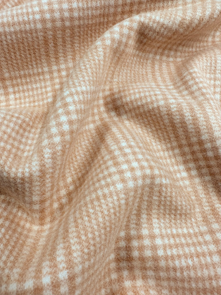 Close-up of a soft, heavy weight fabric draped in gentle folds, featuring a light brown and white houndstooth pattern. The texture appears plush and cozy, suggesting a warm and comfortable material suitable for garments or home decor. This is the Wool Flannel - Mandarin - 148cm by Super Cheap Fabrics.