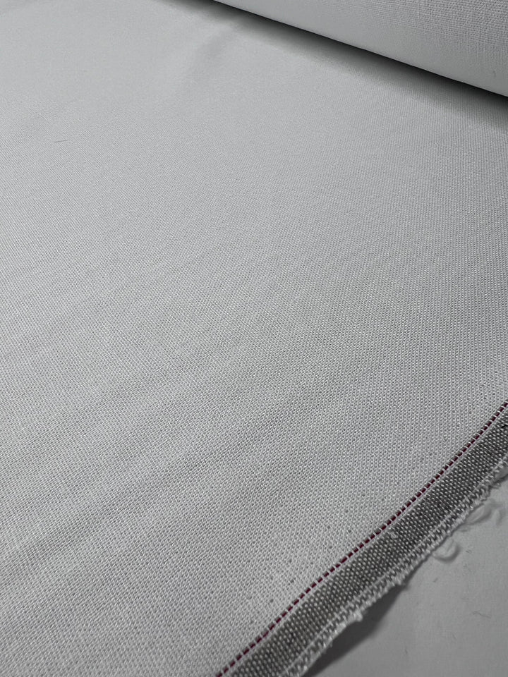 A close-up of the Linen Rayon Blend - White - 137cm by Super Cheap Fabrics shows the light gray fabric's subtle texture, smooth surface, and tightly woven threads, featuring a thin dark line along one edge indicating a seam or selvage.