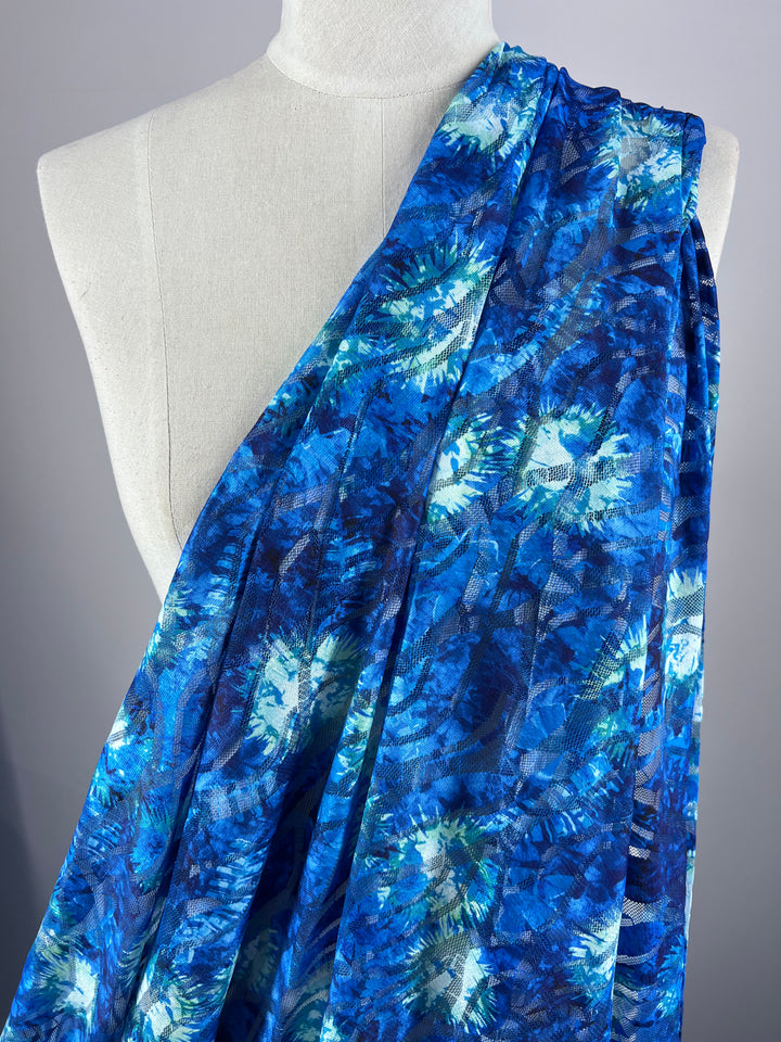 The mannequin showcases the Super Cheap Fabrics' Designer Textured Mesh - Ursula. This lightweight polyester features a vibrant blue and turquoise floral pattern with abstract, swirling designs in varying shades of blue and green.