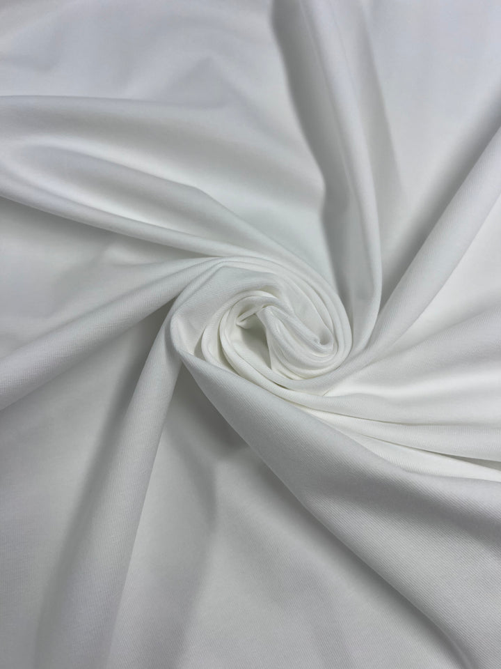 A close-up of Super Cheap Fabrics' Ivory Cotton Lycra (170cm), showcasing its smooth, breathable texture and soft medium-heavy weight in a swirling spiral design.