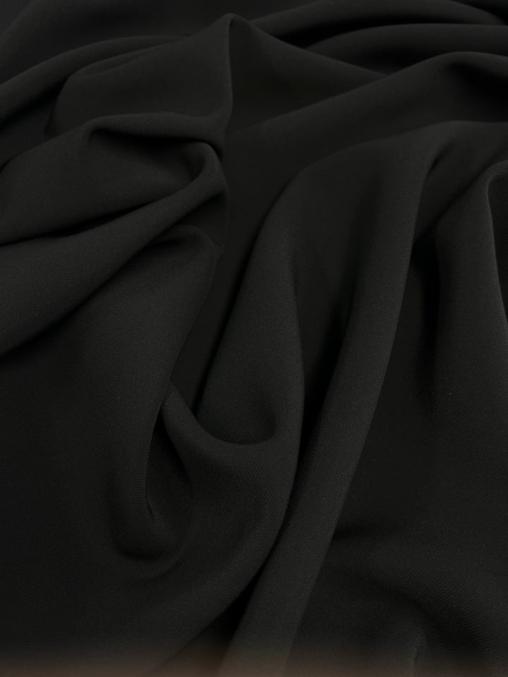 A close-up of Super Cheap Fabrics' Suiting - Saxony Black - 130cm reveals its soft texture, with twill suiting draped in gentle folds to form smooth curves and undulations.