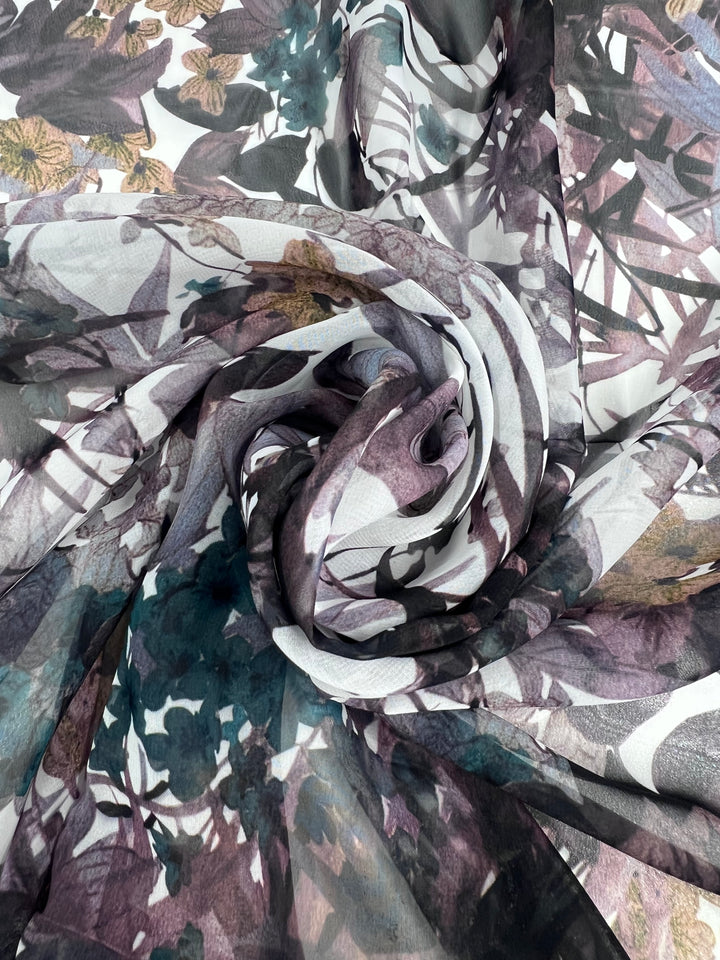 A close-up of Super Cheap Fabrics' Printed Chiffon - Amazonas - 150cm showcases lightweight fabric with a floral and leafy pattern in purple, brown, green, and white. Ideal for sewing projects, its artful swirls create depth and movement.