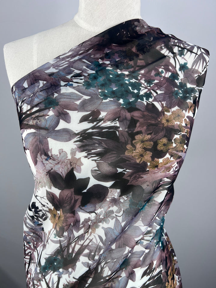 The mannequin is adorned with Super Cheap Fabrics' Printed Chiffon - Amazonas, a 150cm wide lightweight fabric featuring shades of purple, blue, and brown on a gray background. This elegant polyester fabric displays intricate leafy patterns, ideal for sophisticated sewing projects.