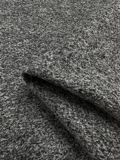 Close-up image of folded, speckled grey Boiled Wool - Charcoal Marle - 140cm by Super Cheap Fabrics with a soft, textured surface. The fabric has a slightly heathered appearance, blending light and dark grey fibers for a subtle, mottled effect. Perfect for autumn/winter clothing, the heavy-weight wool's edges are clearly visible.