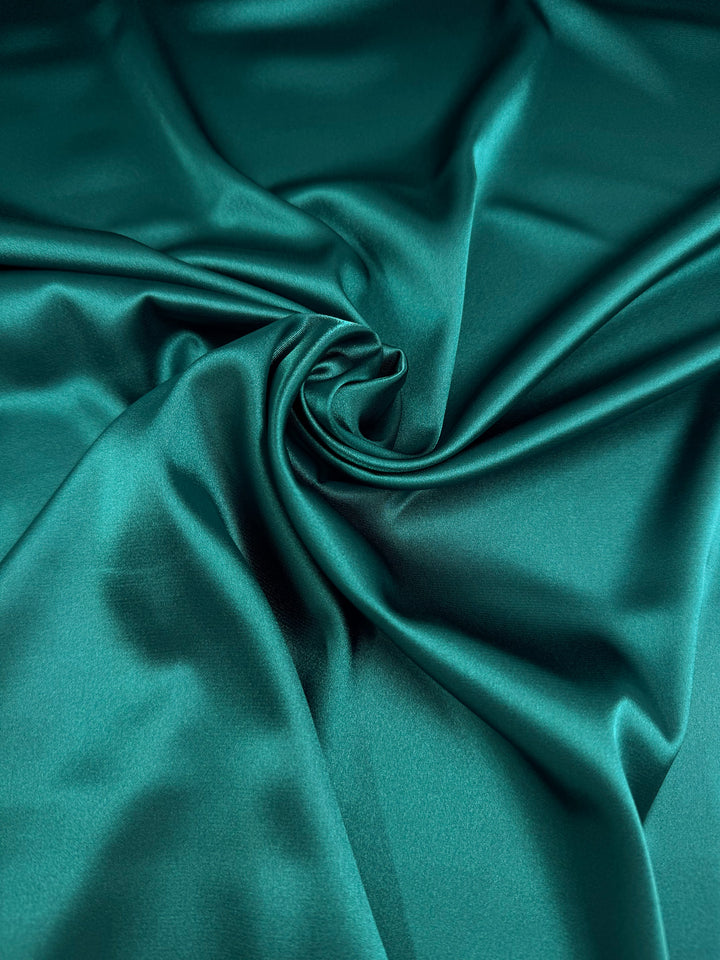 Close-up of Satin Deluxe - Dark Teal (150cm) by Super Cheap Fabrics, showcasing its smooth, shiny finish with gentle folds and a central swirl for a soft, luxurious texture.