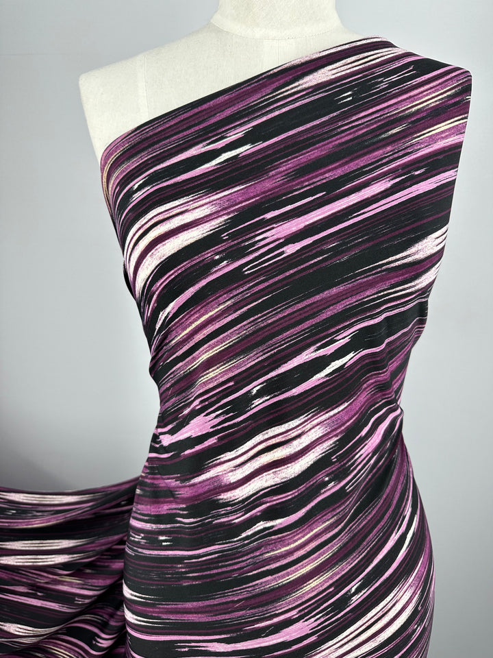 A mannequin is adorned with Super Cheap Fabrics' Printed Lycra - Dashing Lights, featuring a dynamic pattern of pink, black, and white diagonal streaks. This high-contrast design on the medium-weight fabric effortlessly evokes movement against its plain light gray background.