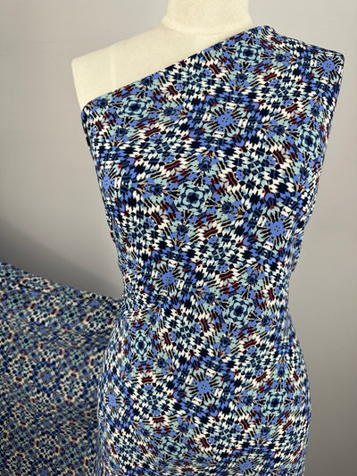 A mannequin showcases Super Cheap Fabrics' "Printed Lycra - Treasure - 150cm," a one-shoulder dress in blue, black, and burgundy geometric patterns on light Polyester/Spandex two-way stretch fabric with intricate kaleidoscope-like designs.