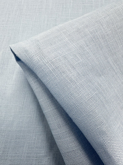 Close-up of neatly folded Pure Linen - Powder Blue from Super Cheap Fabrics, 140cm wide, showcasing a subtle textured pattern. This lightweight linen is soft, finely woven, smooth, breathable, and elegant.