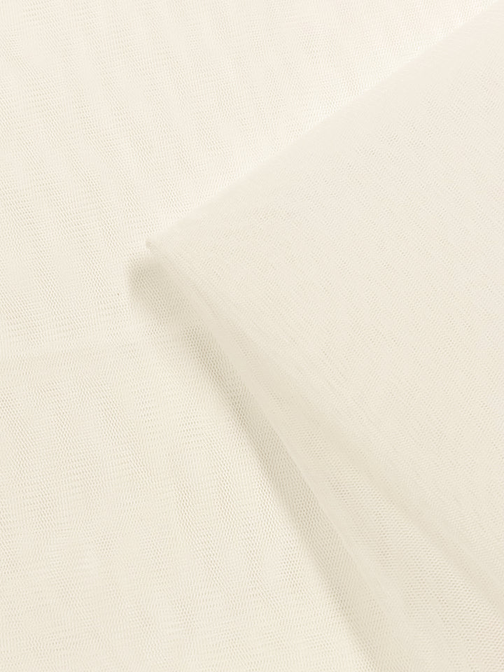 A close-up image of a piece of Soft Tulle - Ivory - 160cm from Super Cheap Fabrics, showcasing its delicate, sheer, and mesh-like texture. The fabric is layered and slightly gathered, emphasizing its soft and airy appearance, perfect for creating elegant dresses with extra lightweight fabric.