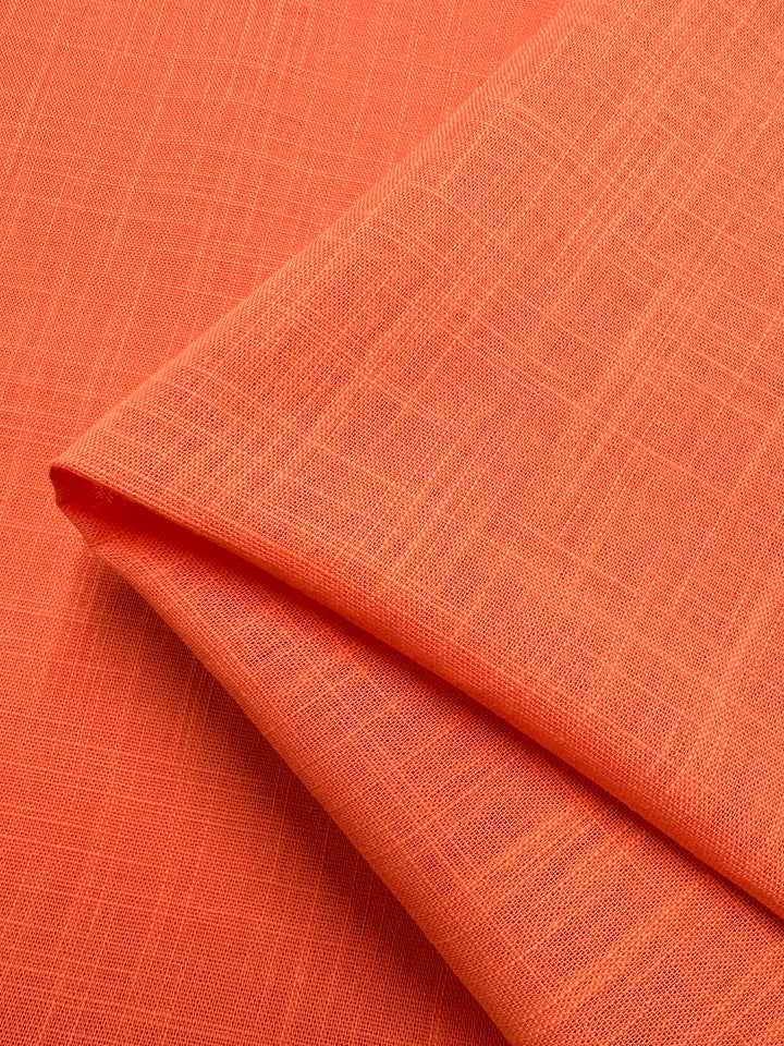 A close-up of the Linen Blend - Camellia - 147cm fabric from Super Cheap Fabrics, showcasing its folded orange texture with a subtle crisscross pattern and neatly arranged woven design. The linen cotton blend appears smooth and elegant.