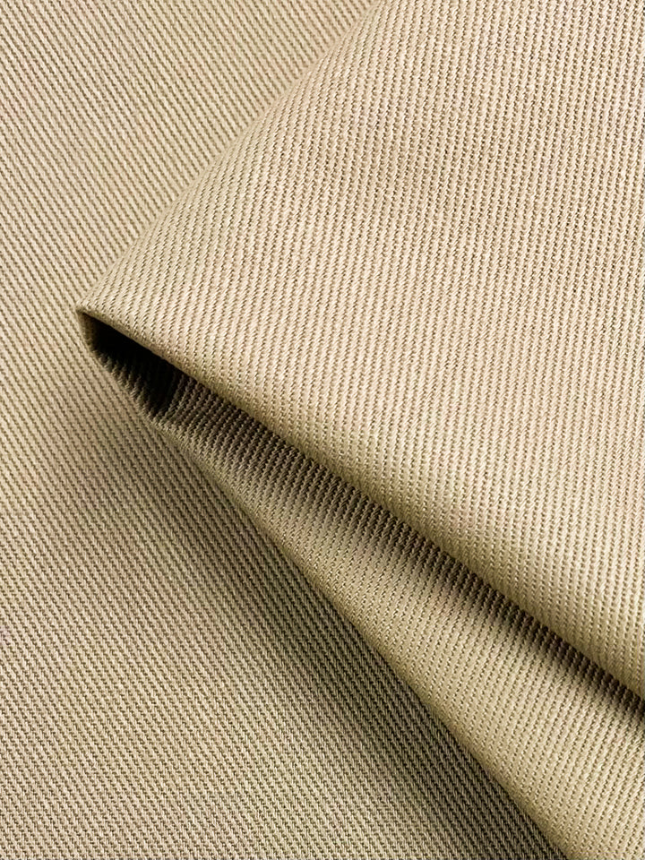 Close-up of folded beige Denim - Cartouche - 150cm fabric with a fine diagonal ribbed texture. The medium weight material appears soft and smooth, showcasing the intricate weave and subtle sheen by Super Cheap Fabrics.