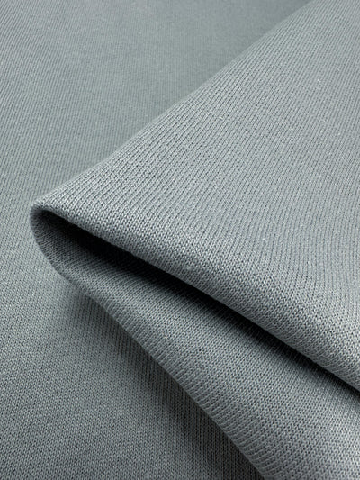 A close-up view of a neatly folded piece of Super Cheap Fabrics' Brushed Fleece in Monument, featuring its light gray hue and showcasing the texture and weave pattern reminiscent of high-quality cotton.