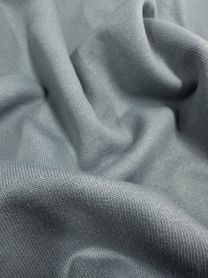 Close-up of soft, light gray Brushed Fleece - Monument from Super Cheap Fabrics with small, fine-knit details. The high-quality cotton fabric is displayed with gentle folds and a mildly textured surface, showcasing its smooth and slightly reflective quality.