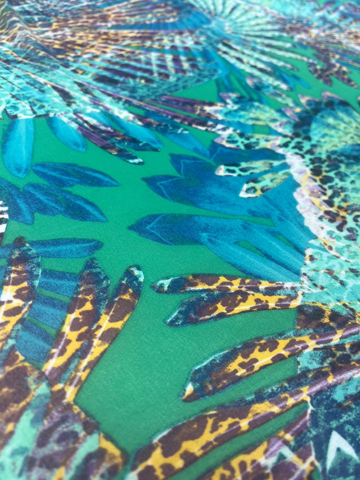 A close-up of a vibrant, extra light-weight fabric pattern with abstract leaf designs in shades of blue, green, and teal, interspersed with animal print and speckles. The intricate design creates a dynamic, tropical feel ideal for fancy dresses in Designer Chiffon - Leopard Palms - 150cm by Super Cheap Fabrics.