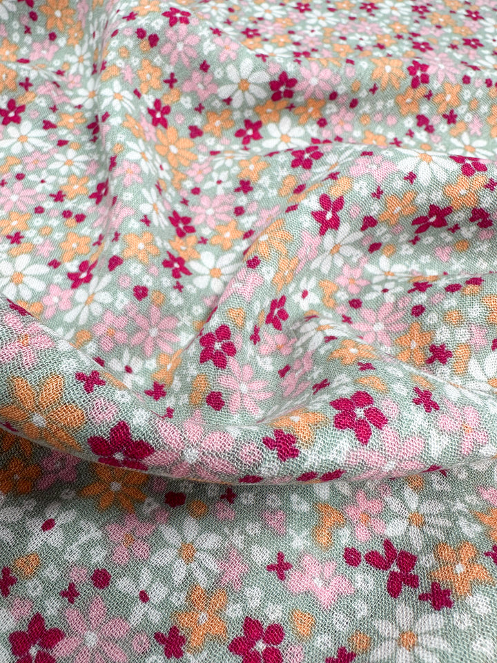 Introducing the Soft Cotton - Cluster - 140cm by Super Cheap Fabrics: This fabric features a vibrant floral design with pink, red, and orange flowers elegantly arranged on a light blue background. The breathable material drapes beautifully, highlighting its lovely texture and pattern—an ideal choice for summer projects.