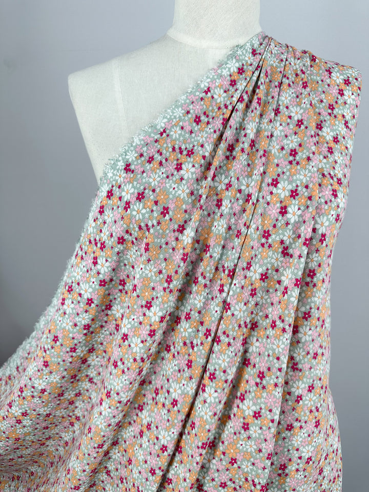 A mannequin adorned with the Soft Cotton - Cluster - 140cm from Super Cheap Fabrics, showcasing a vibrant floral pattern in red, pink, orange, and green hues. Ideal as a breathable summer fabric set against a light gray backdrop.