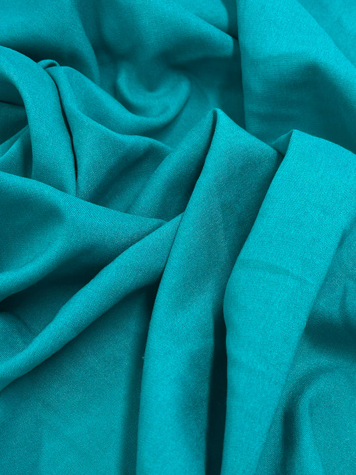 A close-up of Plain Rayon - Columbia - 145cm by Super Cheap Fabrics, featuring crumpled teal fabric with soft folds and creases that highlight its lightweight feel, smooth texture, and vibrant color.